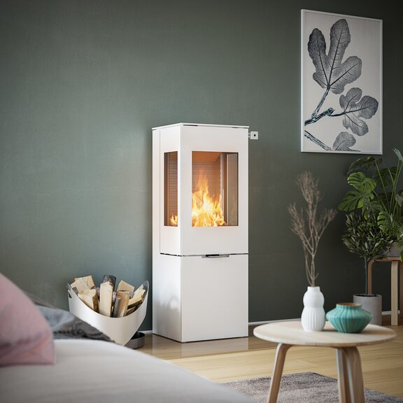 Holz-Kaminofen NEXO 120 in Weiss mit Stahltür und zwei Seitenfenstern vor grüner Wand in dekorativem Wohnraum